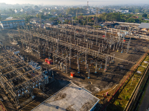Aerial view of an electrical substation with metal structures, power lines, and surrounding urban area in Purwokerto, Central Java, Indonesia.