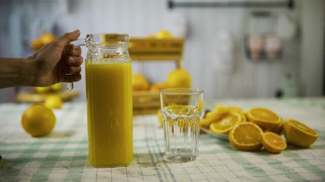 Person pouring orange juice into glass on counter near slices - cinematic slow motion shot