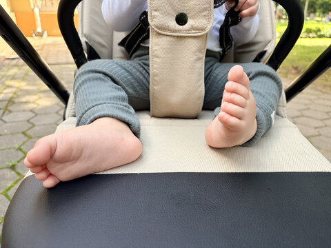 Close-up of a baby's bare feet and legs in a stroller outdoors