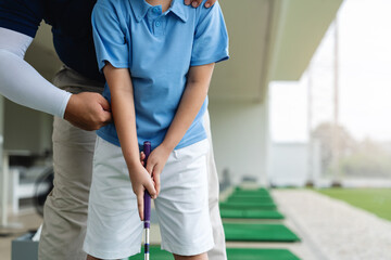 Fototapeta premium Golf Coach correcting an Asian boy's upper body position and grip during a close-up junior golf lesson at a covered driving range practice area