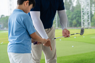 Fototapeta premium Golf Coach guiding an Asian boy through club position and grip technique during a hands-on junior golf lesson at a bright covered driving range