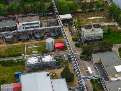 Aerial view of an industrial facility featuring large storage tanks, cooling towers, and complex pipeline networks surrounded by green trees in Breclav, South Moravian Region, Czechia.