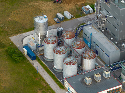 Aerial view of industrial facility with multiple large metal storage silos and adjacent factory buildings situated in a green landscape Breclav, South Moravian Region, Czechia.