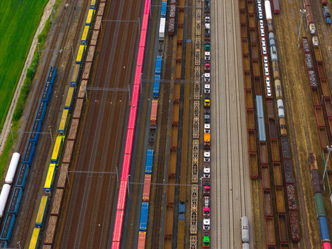 Aerial view of a busy freight train yard with numerous colorful cargo cars parked on parallel tracks next to a green field in Breclav, South Moravian Region, Czechia.