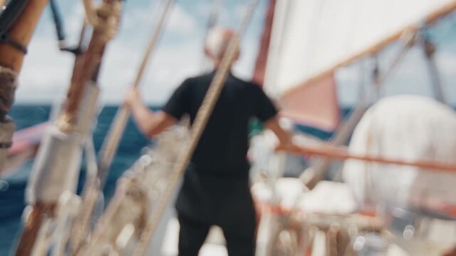 Old captain controls the crew working with the sails on the big expeditional sailing vessel moving in the Atlantic Ocean