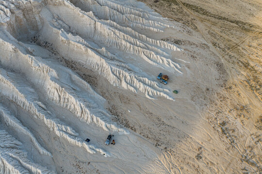 Aerial view of the white chalk formations of Tuzbair with parked vehicles and tents in the desert landscape of Mangystau District, Mangystau Region, Kazakhstan.