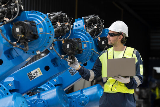 Robotics industry, programming, validation, and monitoring of robotic systems. Male engineer using laptop computer connect to robotics arm system for testing and development solutions