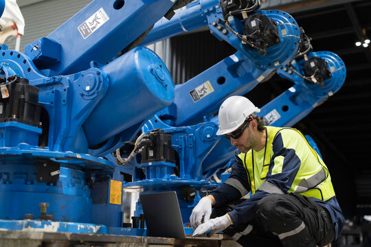 Robotics industry, programming, validation, and monitoring of robotic systems. Male engineer using laptop computer connect to robotics arm system for testing and development solutions
