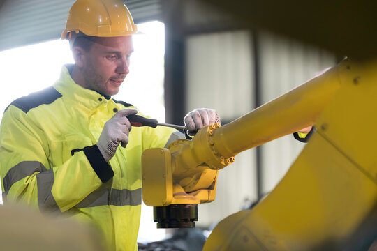 Portrait of male engineer wearing uniform, hard hat and gloves repair automatic robotic arm for welding. Male technician inspecting automatic welding robot arm machine with hand tools