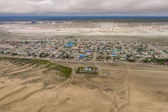 Aerial view of Senek village in the desert landscape of the Mangystau Region, featuring sand dunes, sparse vegetation, and a distant plateau. Senek, Mangystau Region, Kazakhstan.