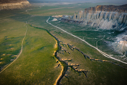 Aerial view of Airakty rock formations rising above the green plains and winding dirt paths in Shetpe, Mangystau Region, Kazakhstan.