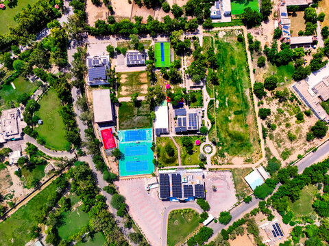 Aerial view of solar power panels installed on building rooftops surrounded by vibrant green lawns, sports courts, and lush trees in Dera Ghazi Khan, Punjab, Pakistan.