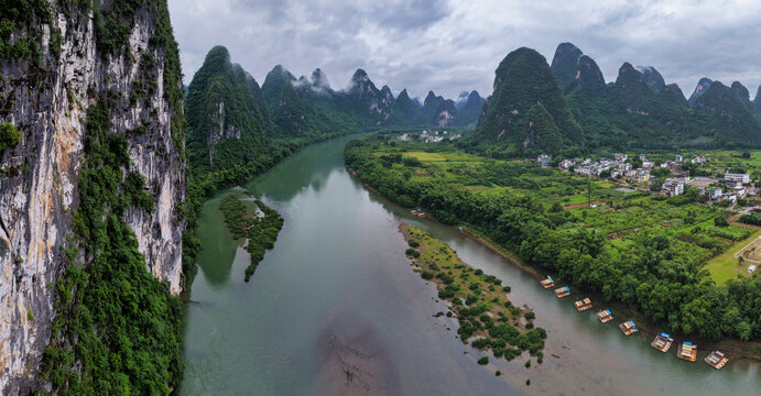Aerial view of the Li River winding through dramatic karst mountains with lush greenery, small villages, and bamboo rafts moored along the riverbank in Guilin, Guangxi, China.
