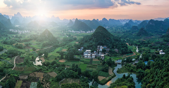 Aerial view of Yangshuo County featuring karst mountains, lush green rice fields, a winding river, and a small village at sunset in Guilin, Guangxi, China.