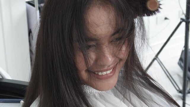 Hair stylist blow drying hair after professional rebonding treatment for Southeast Asian woman in her early 20s