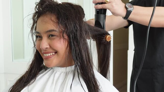 Hair stylist blow drying hair after professional rebonding treatment for Southeast Asian woman in her early 20s
