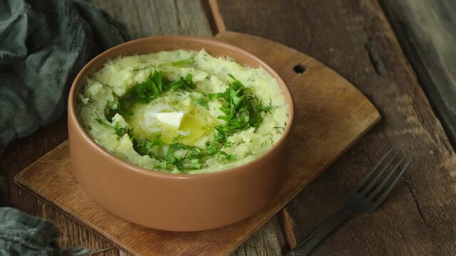 Bowl of mashed potatoes garnished with fresh herbs and butter on wooden table