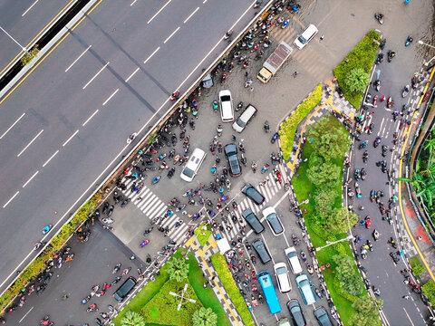 Aerial view of Jalan Outer Ring Road intersection with heavy traffic of cars and motorcycles, surrounded by trees in Kecamatan Cengkareng, Daerah Khusus Ibukota, Indonesia.