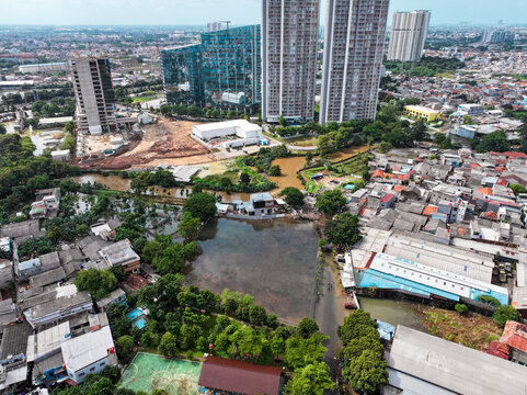 Aerial view of a flooded residential area near SDN Kembangan Utara 2 PT3 PG, with modern high-rise buildings in the background, Kecamatan Kembangan, Daerah Khusus Ibukota, Indonesia.