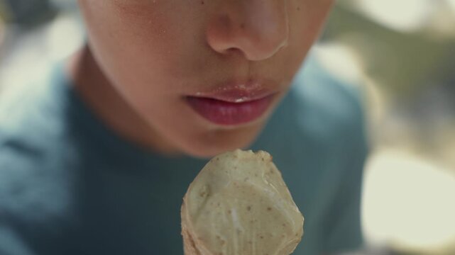 Close-up of a young boy licking a tasty pistachio ice cream cone outdoors on a sunny day, enjoying a sweet summer snack with pleasure and savoring every single bite
