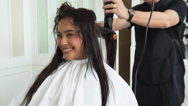 Hair stylist blow drying hair after professional rebonding treatment for Southeast Asian woman in her early 20s