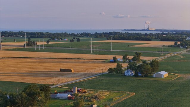 Aerial view of the rural landscape featuring golden wheat fields, green crops, farm buildings, and the distant Monroe Power Plant in Frenchtown Township, Michigan, United States.