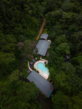 Aerial view of a secluded resort nestled in a lush rainforest, featuring a turquoise swimming pool, modern buildings, and dense tropical vegetation in Alajuela Province, Costa Rica.