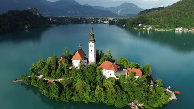 Cinematic aerial drone flight toward Bled Island and the Church of the Assumption on Lake Bled, Slovenia, showcasing the iconic island surrounded by emerald water.