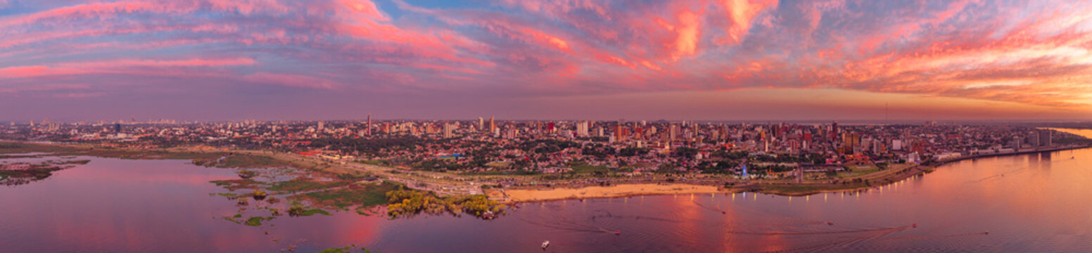 Aerial view of the skyline of Asuncion along the Paraguay River at sunset, with vibrant clouds reflecting over the water and urban buildings in Asuncion, Asuncion, Paraguay.