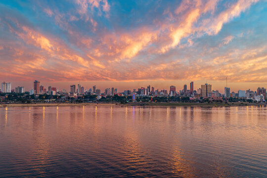 Aerial view of the Costanera Norte waterfront and the Asuncion skyline at sunset with calm river waters and a vibrant sky in Asuncion, Asuncion, Paraguay.
