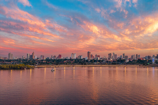 Aerial view of the Asuncion skyline at sunset with the Costanera Norte waterfront, reflecting vibrant orange and pink clouds over the Paraguay River, Asuncion, Asuncion, Paraguay.