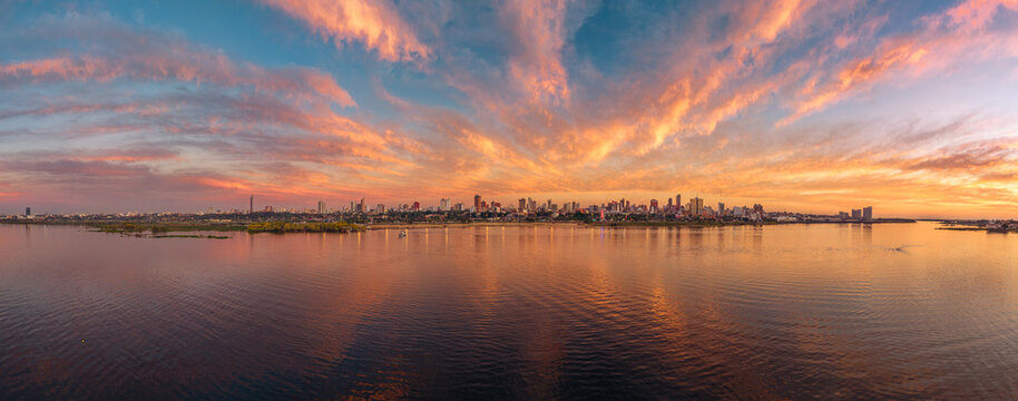 Aerial view of Costanera Norte waterfront and Asuncion skyline under a vibrant sunset with clouds reflecting on the Paraguay River. Asuncion, Asuncion, Paraguay.
