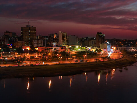 Aerial view of Costanera Norte at night with the illuminated skyline of Asuncion reflecting on the Paraguay River, featuring urban lights in Asuncion, Asuncion, Paraguay.