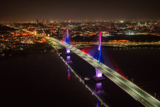 Aerial view of Puente Heroes del Chaco illuminated at night with vibrant red and blue lights, spanning the Paraguay River with the city skyline in the background, Asuncion, Paraguay.