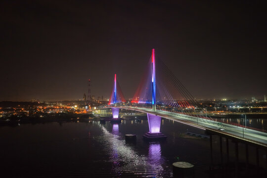 Aerial view of the illuminated Puente Heroes del Chaco bridge at night, with vibrant lights reflecting on the Paraguay River and the city skyline in the background. Asuncion, Paraguay.