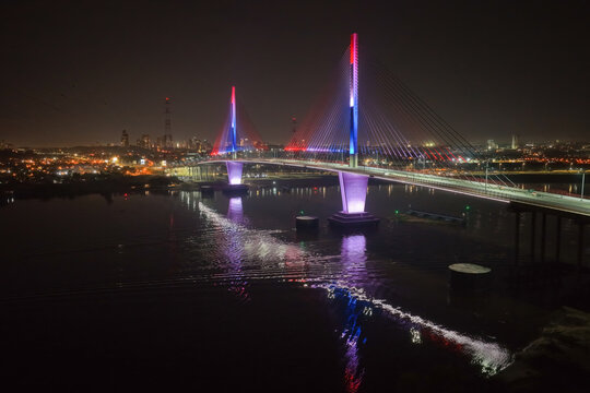 Aerial view of the illuminated Puente Heroes del Chaco bridge spanning the Paraguay River at night, with vibrant red, white, and blue lighting reflecting on the water in Asuncion, Paraguay.