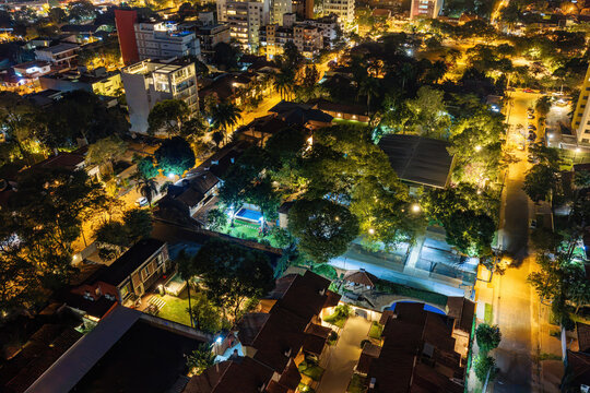 Aerial view of the Las Lomas neighborhood at night with illuminated residential streets, lush trees, and urban architecture in Asuncion, Asuncion, Paraguay.