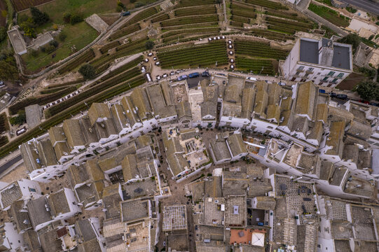 Aerial view of the historic white stone buildings and narrow streets of the old town surrounded by terraced vineyards in Locorotondo, Apulia, Italy.