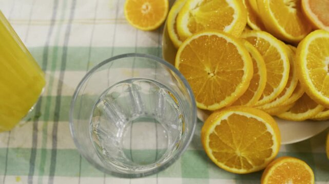 Juice being poured into glass near orange slices - closeup, high, slow motion shot