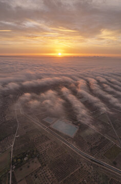 Aerial view of the landscape of Ginosa at sunset, with a reservoir surrounded by agricultural fields and a sea of clouds under a golden sky, Ginosa, Apulia, Italy.