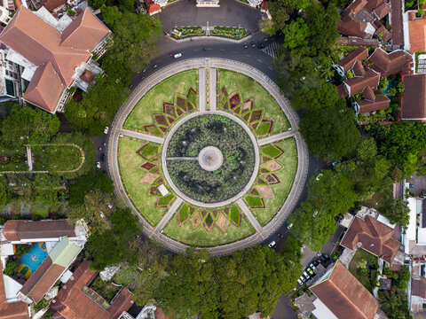 Aerial view of Alun Alun Tugu Malang, a circular park featuring a central fountain and lotus pond surrounded by lush trees and historic colonial architecture in Malang, East Java, Indonesia.