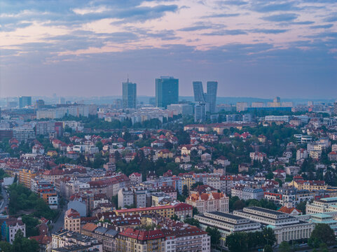 Aerial view of the Prague skyline featuring modern skyscrapers like the V Tower and City Tower rising above historic residential rooftops and lush green trees in Prague, Prague, Czechia.