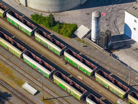 Aerial view of freight train cars parked on parallel tracks in an industrial rail yard with storage silos and concrete structures in Prague, Prague, Czechia.