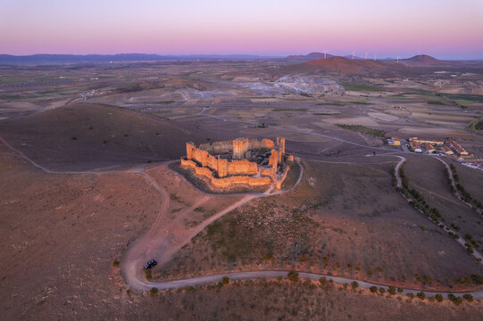 Aerial view of Castle Almonacid of Toledo ruins illuminated by golden hour light, surrounded by rolling hills and fields in Almonacid de Toledo, Castilla-La Mancha, Spain.