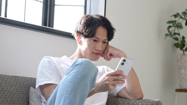 リビングでスマートフォンを見ながらくつろぐ30代の日本人男性
