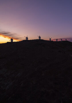 Aerial view of the historic Molinos de Viento de Consuegra silhouetted against a vibrant sunset sky on a ridge in Consuegra, Castilla-La Mancha, Spain.