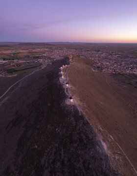 Aerial view of the historic Molinos de Viento de Consuegra windmills perched on a ridge overlooking the town at sunset with soft purple light in Consuegra, Castilla-La Mancha, Spain.