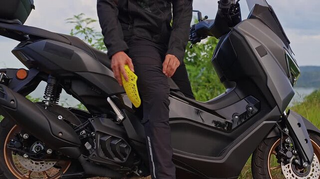 Motorcyclist Inserts Yellow Knee Armor Into Protective Riding Pants Beside a Scooter Outdoors, Supporting Rider Preparation and Injury Prevention