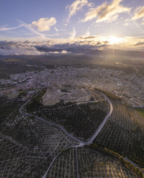 Aerial view of the historic Fortaleza de la Mota fortress perched on a hill overlooking the town surrounded by vast olive groves at sunset in Alcala la Real, Andalucia, Spain.