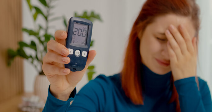 A woman looks shocked as she shows her glucometer reading of 200 mg dL. This high blood sugar level raises concern about her health and diabetes management.